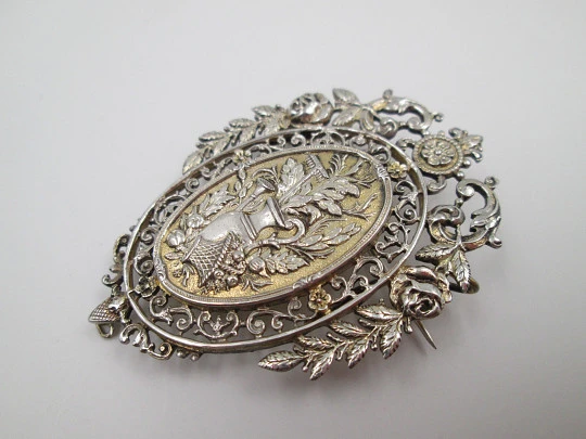 Broche mujer. Metal blanco y dorado. Cerco calado floreado. Cántaro y cesta. 1950